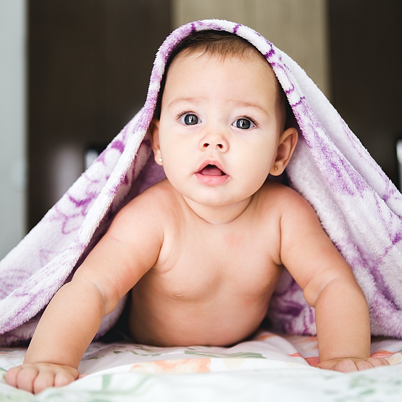A cute baby partially covered by a purple blanket.